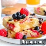 Two sheet pan pancakes cut into squares stacked on a white plate and topped with with fresh berries and maple syrup.
