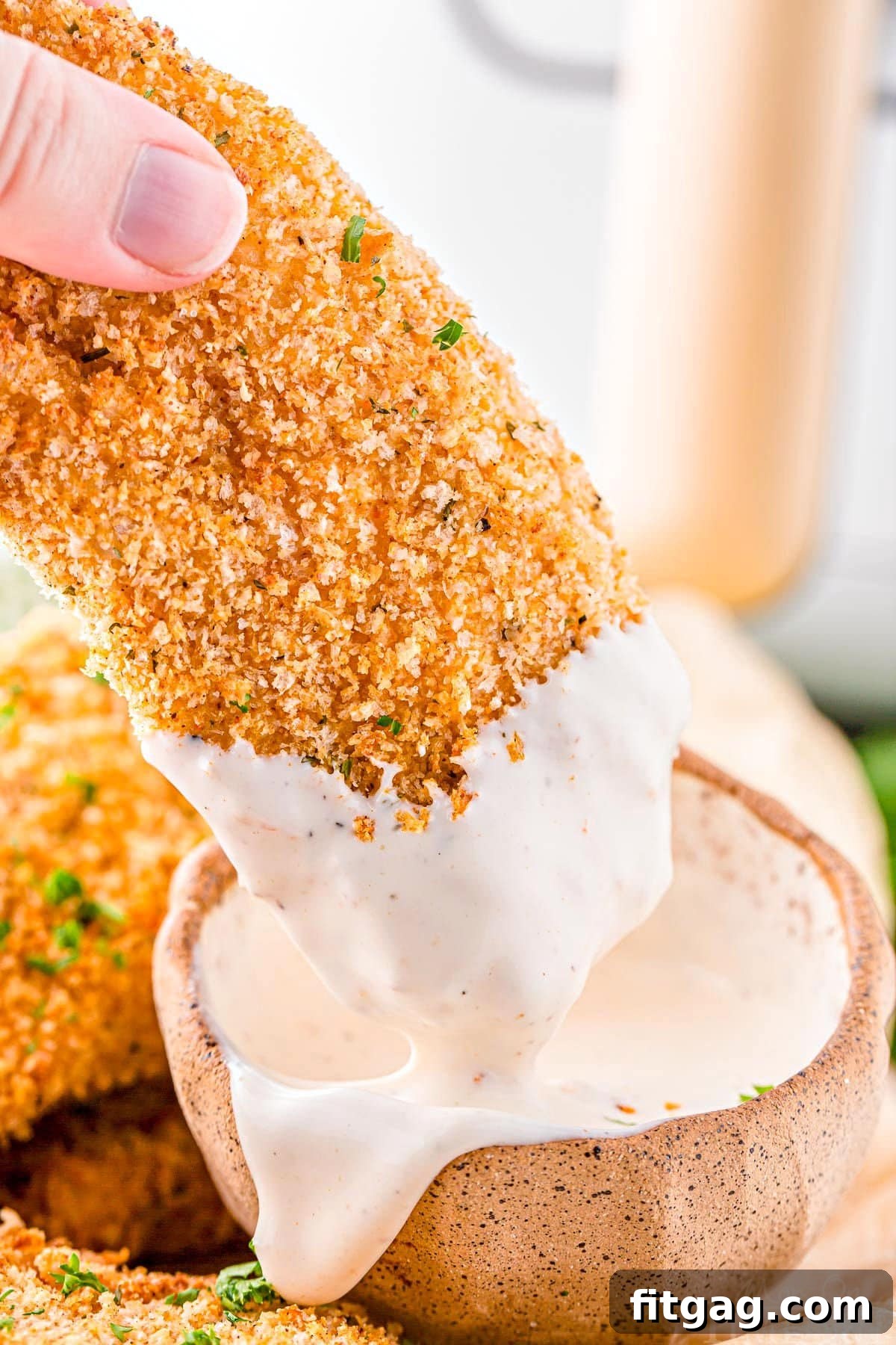 Crispy air fryer chicken tender being dipped into a small bowl of fry sauce, highlighting its golden-brown exterior.
