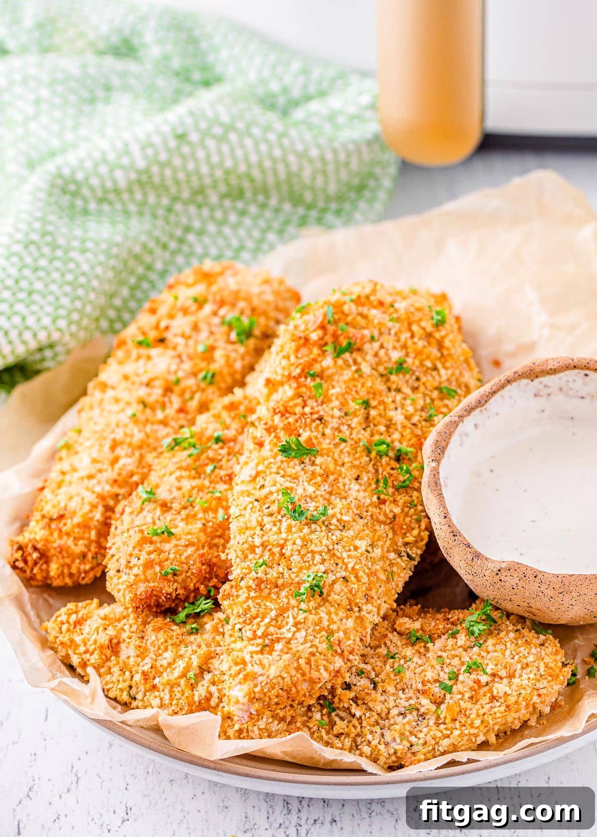 Golden-brown air fryer chicken tenders beautifully plated and garnished with parsley, with the air fryer in the background.