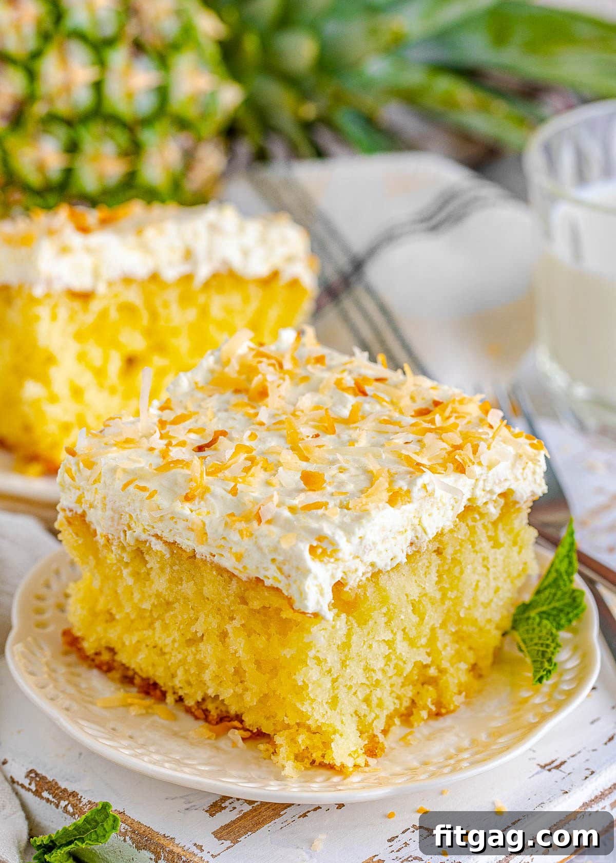A single, inviting piece of Pina Colada Poke Cake rests on a white plate, perfectly ready to be savored. It's crowned with a lavish, fluffy pineapple coconut frosting and generously sprinkled with golden toasted shredded coconut, promising a delightful tropical escape.