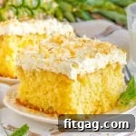 square piece of pina colada cake on a white plate frosted with white frosting and toasted coconut. a pineapple and another piece of cake can be seen in the background.