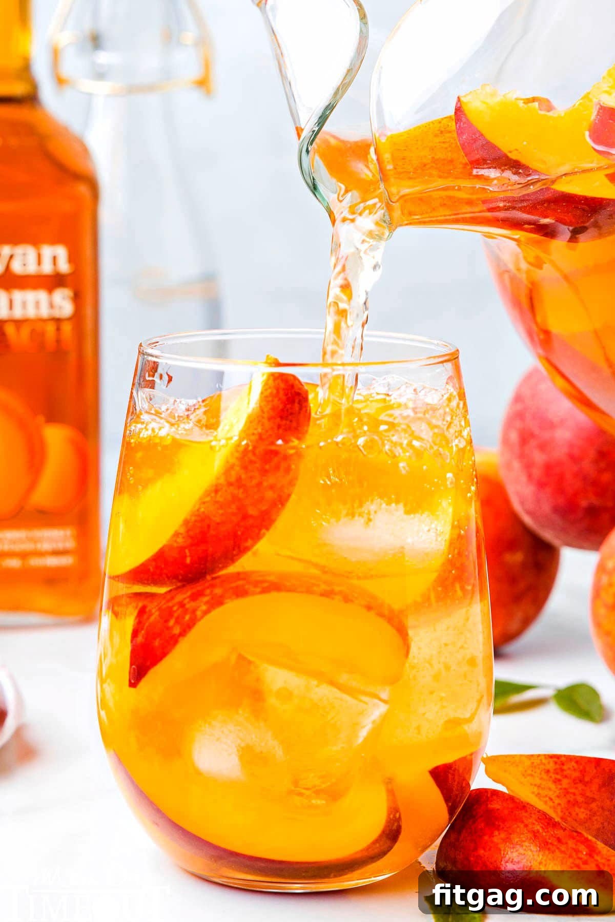 Golden Peach Sangria 2 peach sangria being poured into a short glass that has peach slices and ice in it.