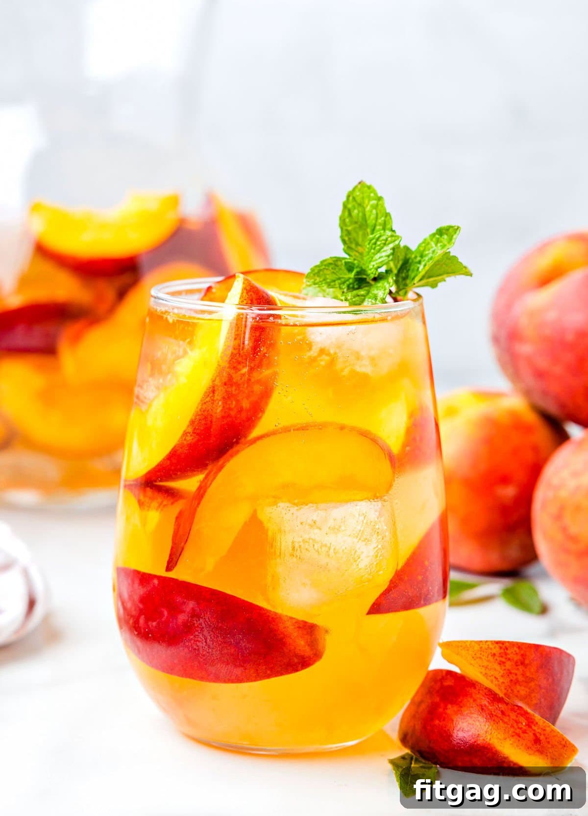 Golden Peach Sangria 7 peach sangria recipe made with white wine in stemless wine glass ready to be enjoyed. garnished with mint and fresh peach slices.