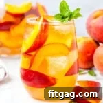 Golden Peach Sangria 8 peach sangria recipe made with white wine in stemless wine glass ready to be enjoyed. garnished with mint and fresh peach slices.