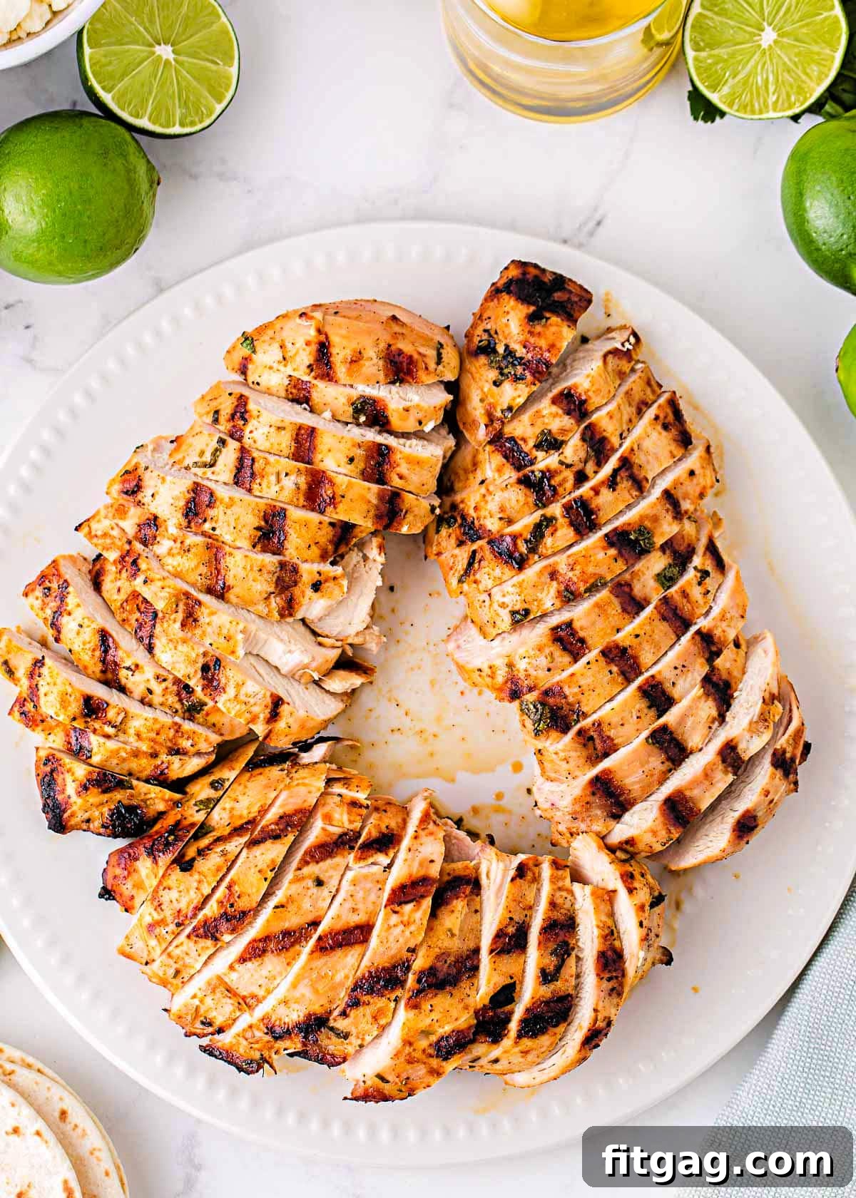 white plate with grilled chicken breasts cut into slices arranged in a circular pattern. Limes can be seen next to the plate.
