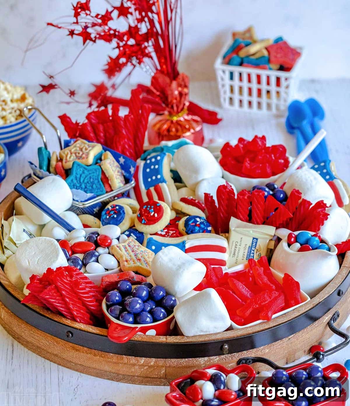 Stars and Stripes Grazing Board 3 An angled front view of a round wooden dessert board, lavishly adorned with an assortment of red, white, and blue holiday treats including marshmallows, cookies, and various candies, creating a festive display.