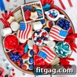 A top-down view of a wooden charcuterie board brimming with red, white, and blue desserts for the 4th of July, featuring cookies, candies, and a variety of colorful treats.