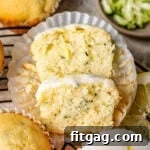 A lemon zucchini muffin sliced in half with three whole muffins, fresh lemon slices, and shredded zucchini artfully arranged nearby.