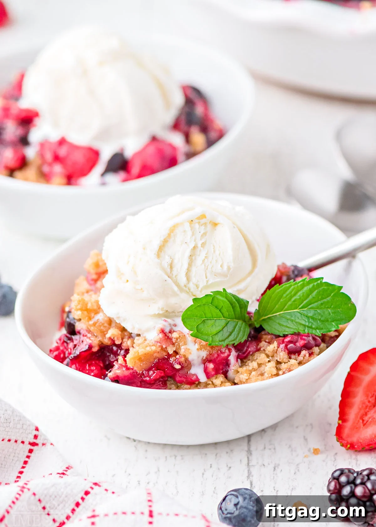 Two bowls of berry crumble topped with a scoop of vanilla ice cream, served in white bowls.