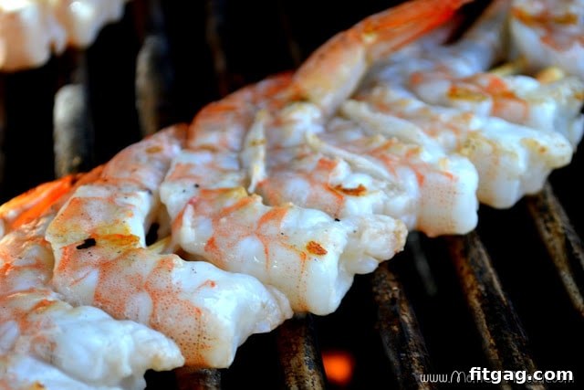 Cooked, bright pink shrimp being removed from the grill with tongs