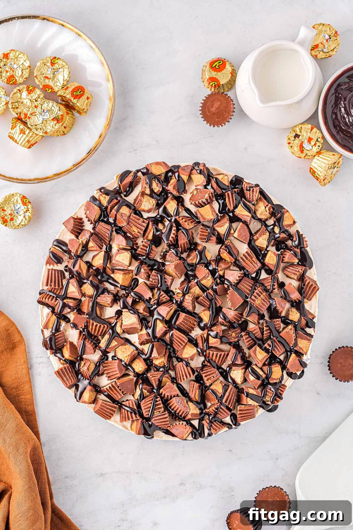 A beautiful top-down view of a whole peanut butter cheesecake, artfully adorned with Reese's candies and a rich hot fudge drizzle, poised for slicing and enjoyment.