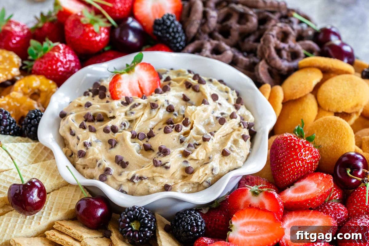 Decadent Cookie Dough Dip 3 A vibrant front view of a white bowl generously filled with delectable chocolate chip cookie dough dip, beautifully surrounded by an inviting array of various dippers, including crisp cookies and fresh, colorful fruit slices.