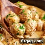 four meatballs on a wooden spoon being scooped out of skillet with the rest of the swedish meatballs and sauce.