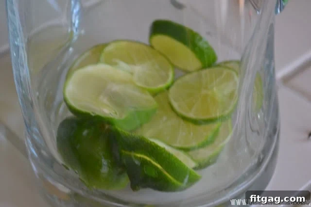 Thinly sliced fresh limes arranged at the bottom of a clear glass pitcher.