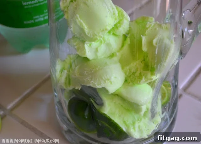 Scoops of vibrant green lime sherbet being added to a pitcher with lime slices.
