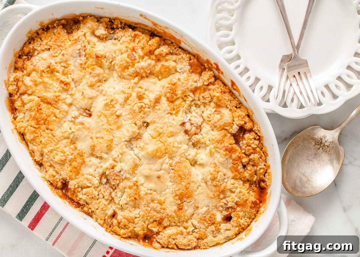 No-Fuss Apple Cobbler 3 A freshly baked easy apple cobbler in a white ceramic baking dish, with two empty white plates and forks positioned neatly beside it, suggesting it's ready to be served.