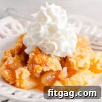scoop of apple cobbler served on a white lace edged plate topped with fresh whipped cream. white casserole dish with remaining cobbler in the background.