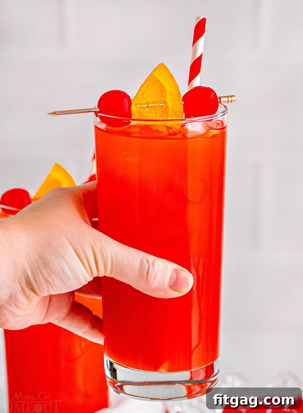 Southern Knockout 6 A vibrant Alabama Slammer cocktail held up against a blurred background, featuring a red and white striped straw and garnished with a maraschino cherry and an orange slice.