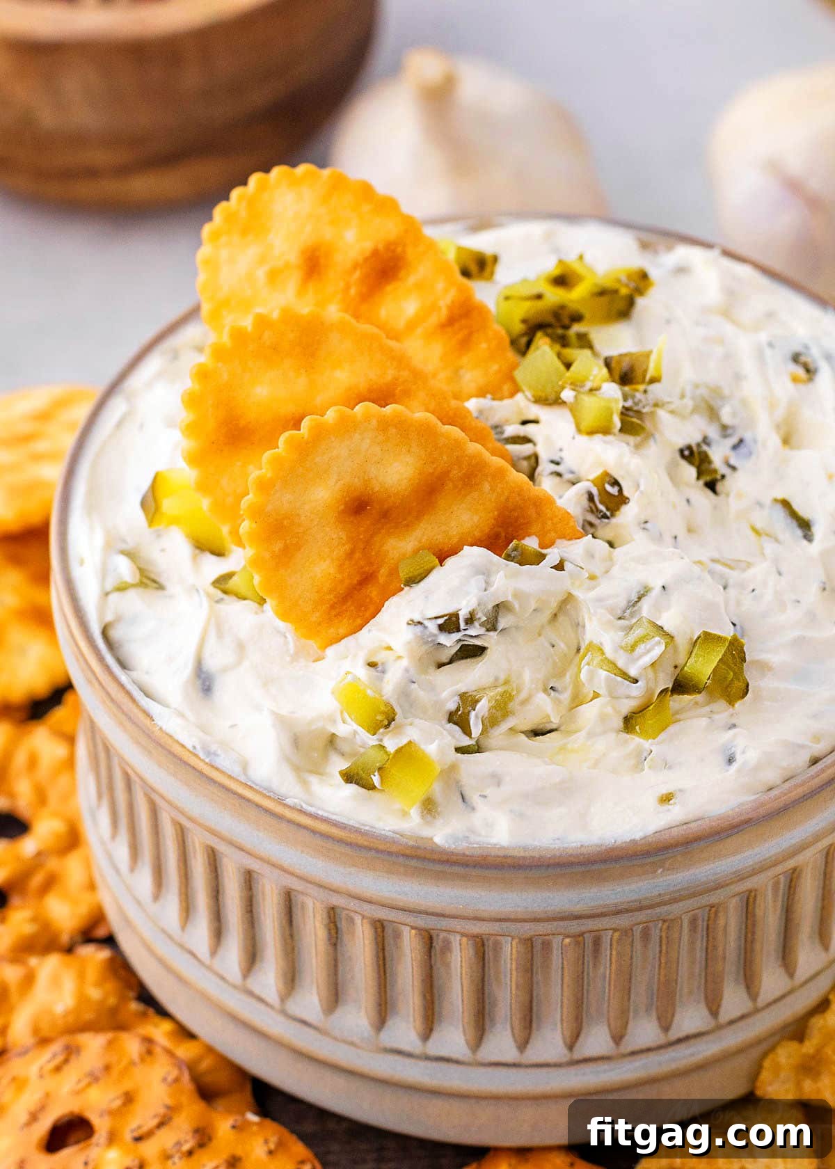 Creamy Dill Pickle Dip 2 small clay bowl with dill pickle dip in it. three crackers are dipped into the dip with a sprinkle of chopped pickle scattered on top.