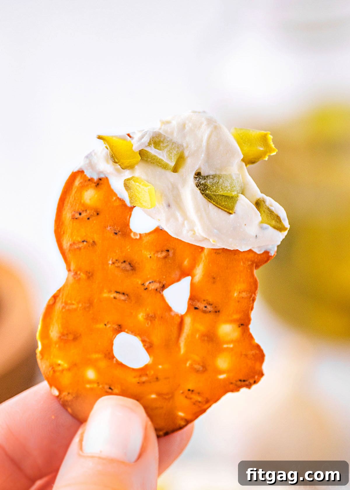 Creamy Dill Pickle Dip 3 pretzel chip is being held up with dill pickle dip on the end of the pretzel.