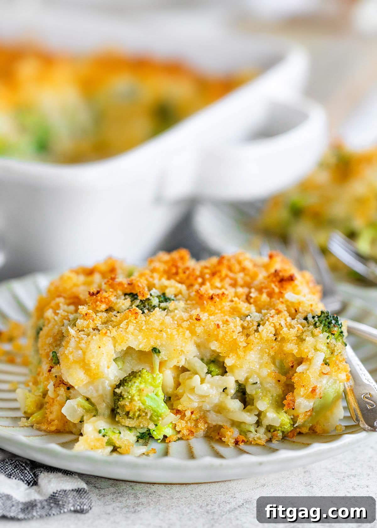 serving of broccoli rice casserole on a small decorative white plate with the casserole dish in the background.