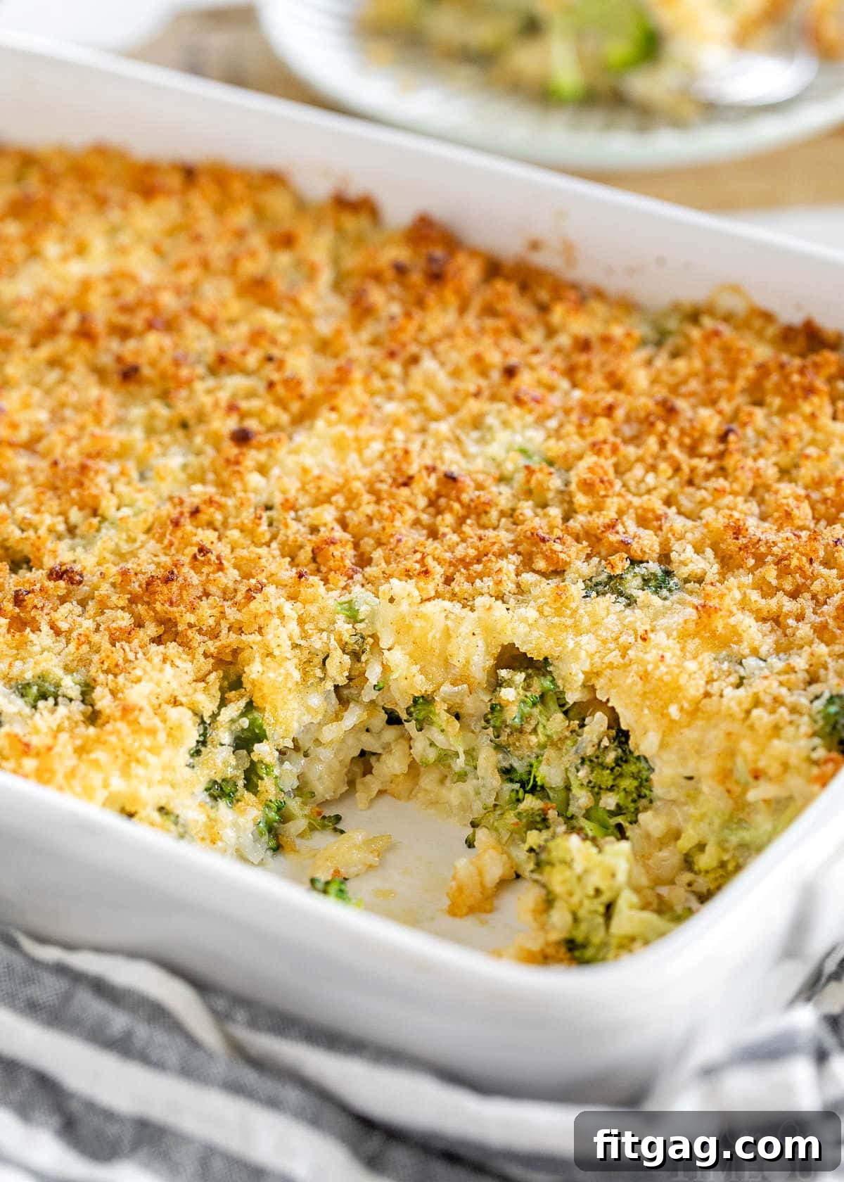 white casserole dish with broccoli rice casserole recipe in it. scoop of the casserole has been removed and is on a small white plate in the background.