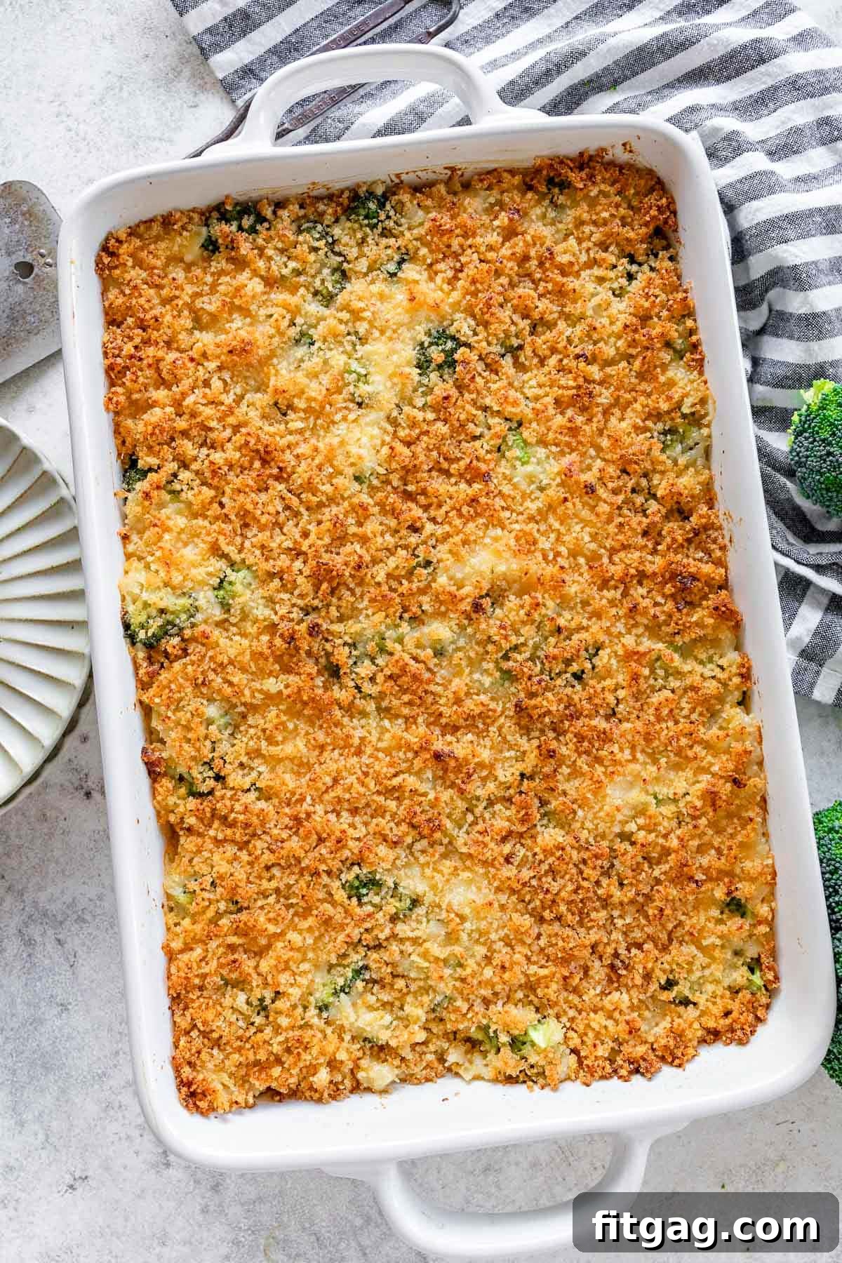 top down look at broccoli rice cheese casserole in a white baking dish next to a black and white striped towel.
