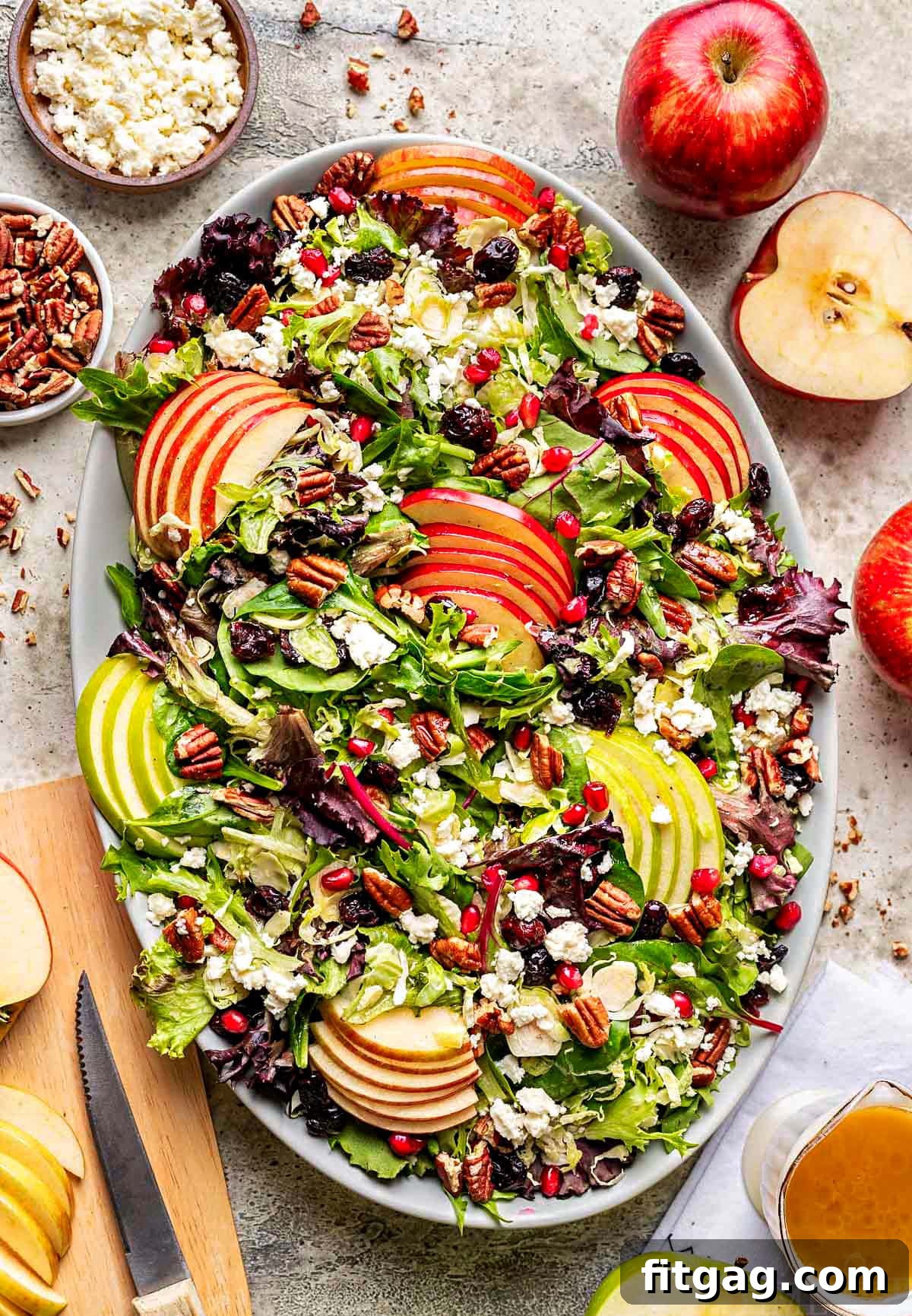 top down look at apple salad made with brussels sprout, apples, cranberries and topped with a vinaigrette. oval serving bowl is sitting on a gray surface with cut apples around it.