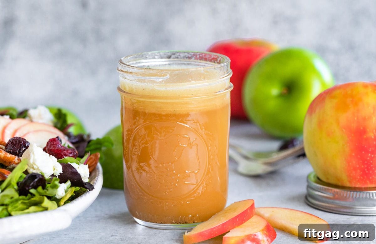 apple vinaigrette in small mason jar sitting next to a salad with apples in background.