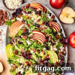 top down look at apple salad made with brussels sprout, apples, cranberries and topped with a vinaigrette. oval serving bowl is sitting on a gray surface with cut apples around it.