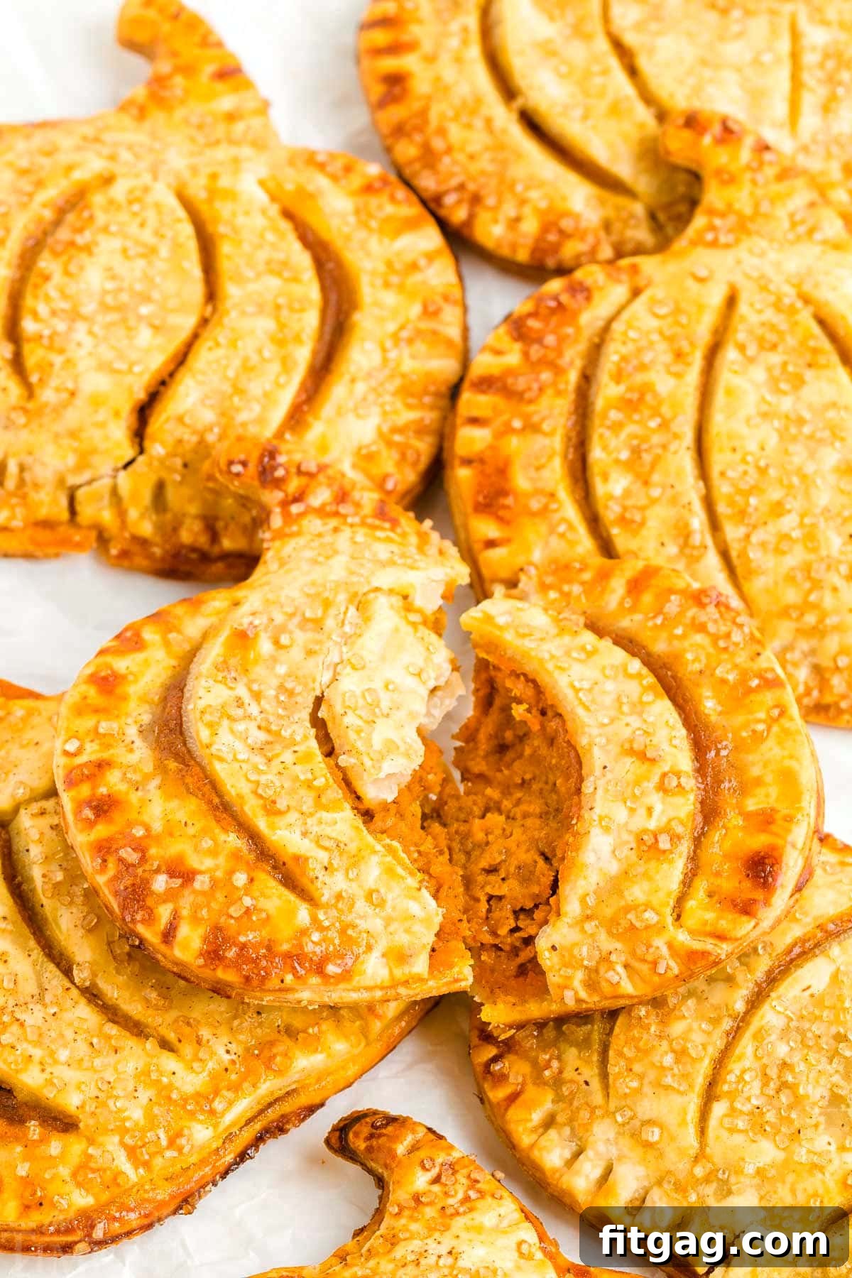 Pumpkin Pie Pockets 6 A pumpkin hand pie split in half to reveal its creamy pumpkin filling, resting on a plate alongside more whole pumpkin pies.