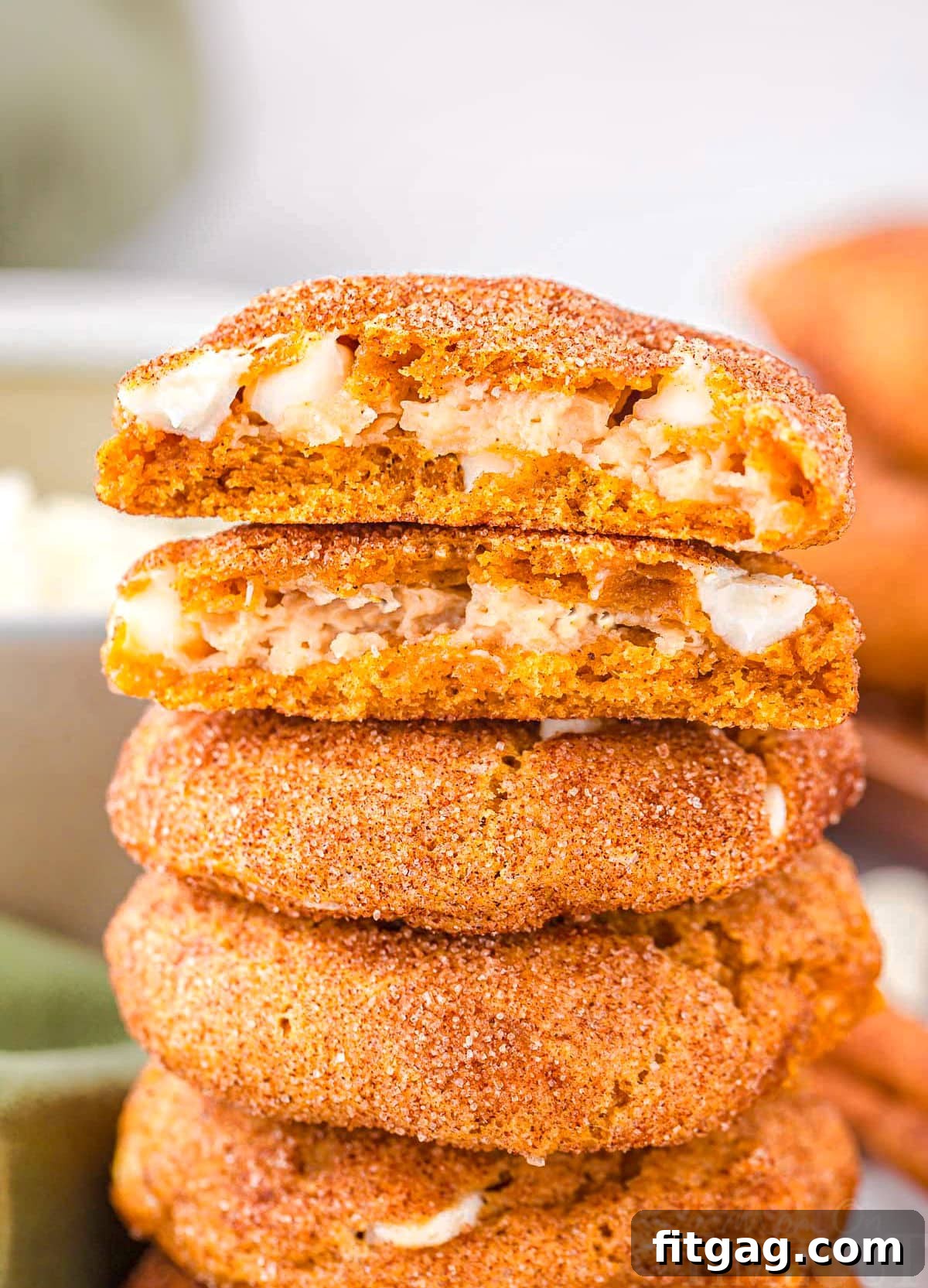 A stack of perfectly baked pumpkin snickerdoodle cheesecake cookies, with the top cookie expertly torn in half to reveal its decadent, creamy cheesecake filling. The rich orange hue of the pumpkin cookie contrasts beautifully with the pale, smooth filling, making it an irresistible visual treat for fall baking.