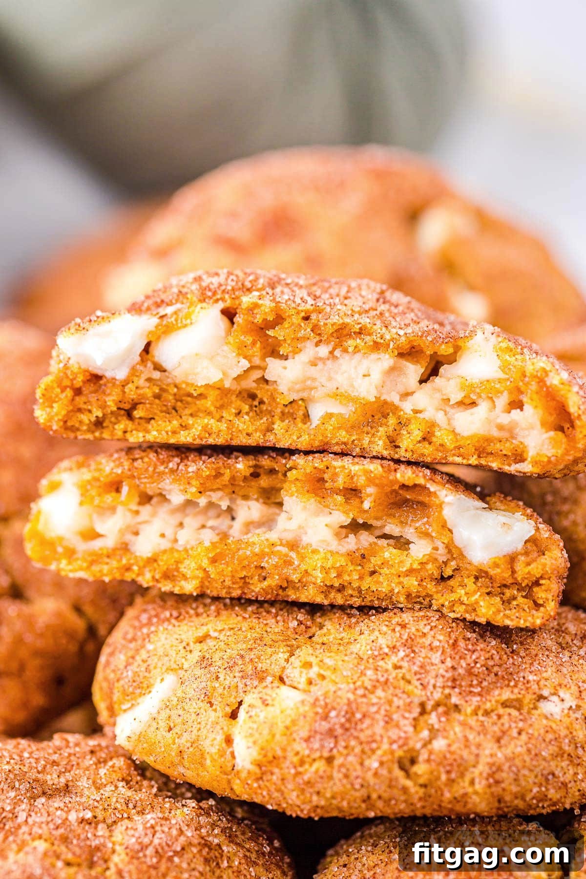 A close-up view of two pumpkin snickerdoodle cheesecake cookies stacked, with the top one broken open to showcase the creamy, white cheesecake filling against the warm, spiced pumpkin cookie interior. The image highlights the perfect texture and delicious surprise inside.