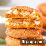 pumpkin snickerdoodle cookies stuffed with cheesecake filling stacked on top of each other with the top cookie torn in half so you can see the filling.