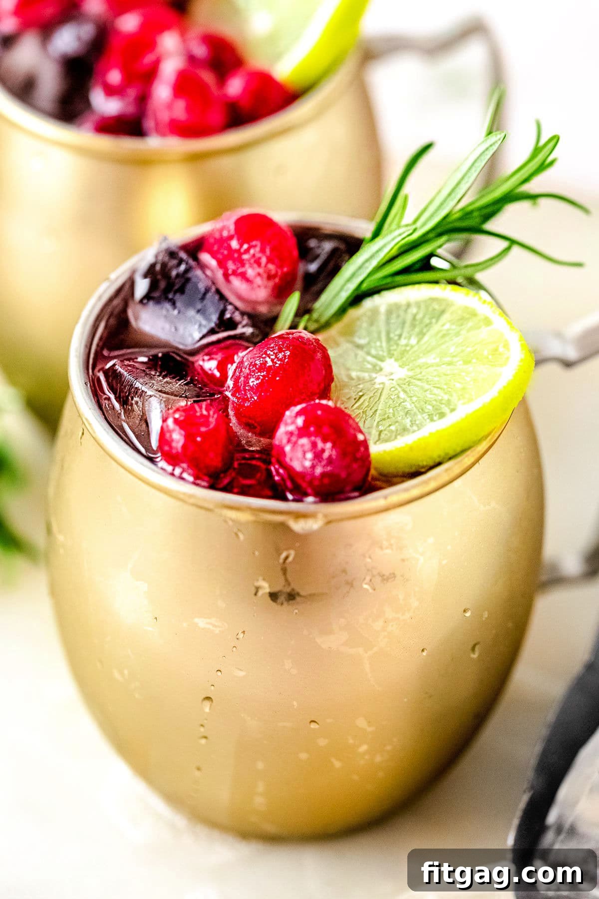 Crimson Moscow Mule 3 A close-up view of the garnishes on a Cranberry Moscow Mule, with another cocktail blurred in the background, highlighting the fresh cranberries, lime, and rosemary.