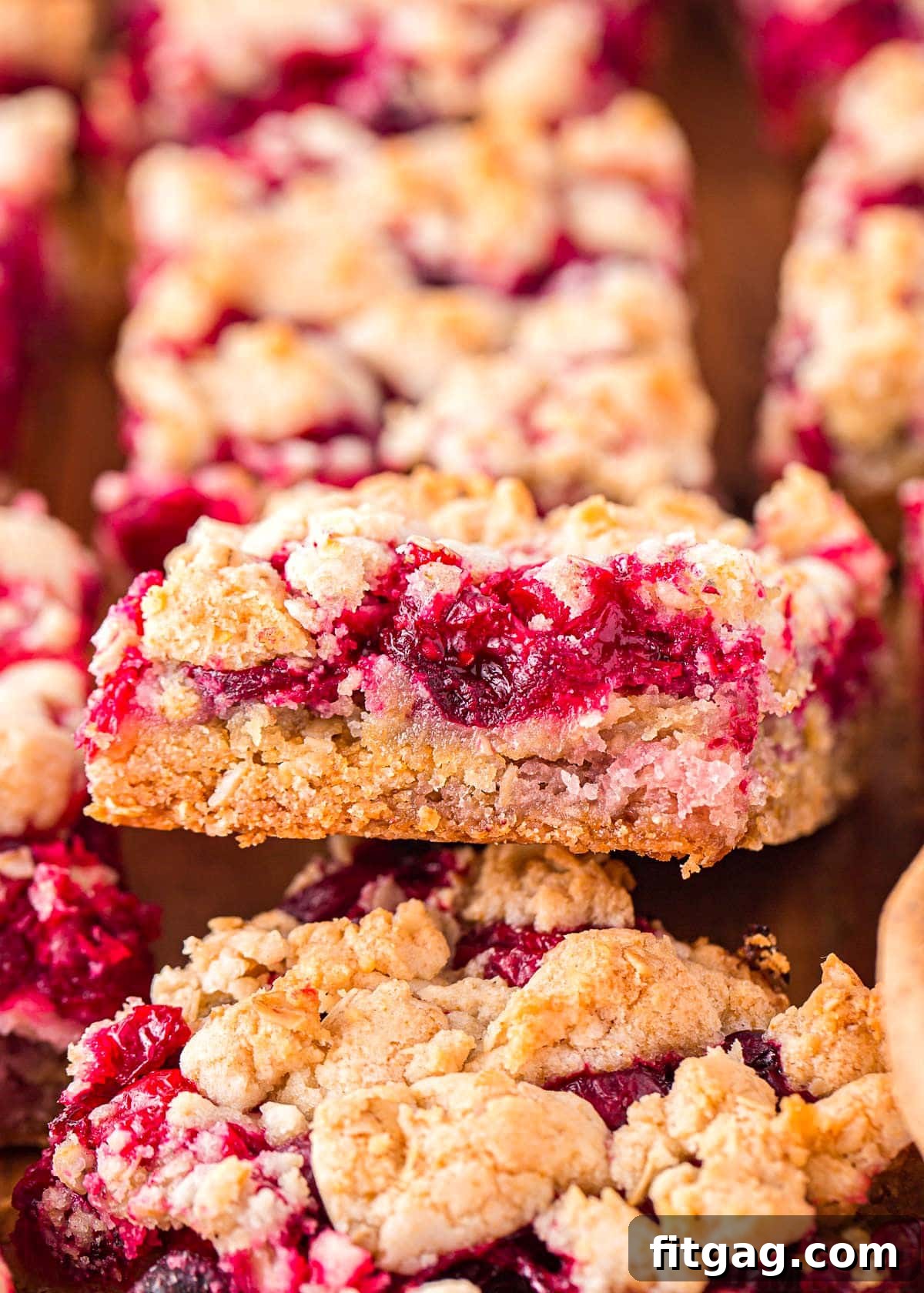 Cranberry bars on a wood board with the center bar flipped up so the filling takes center stage and you can see the profile of the bar, showcasing the vibrant cranberry layer and crumbly topping.
