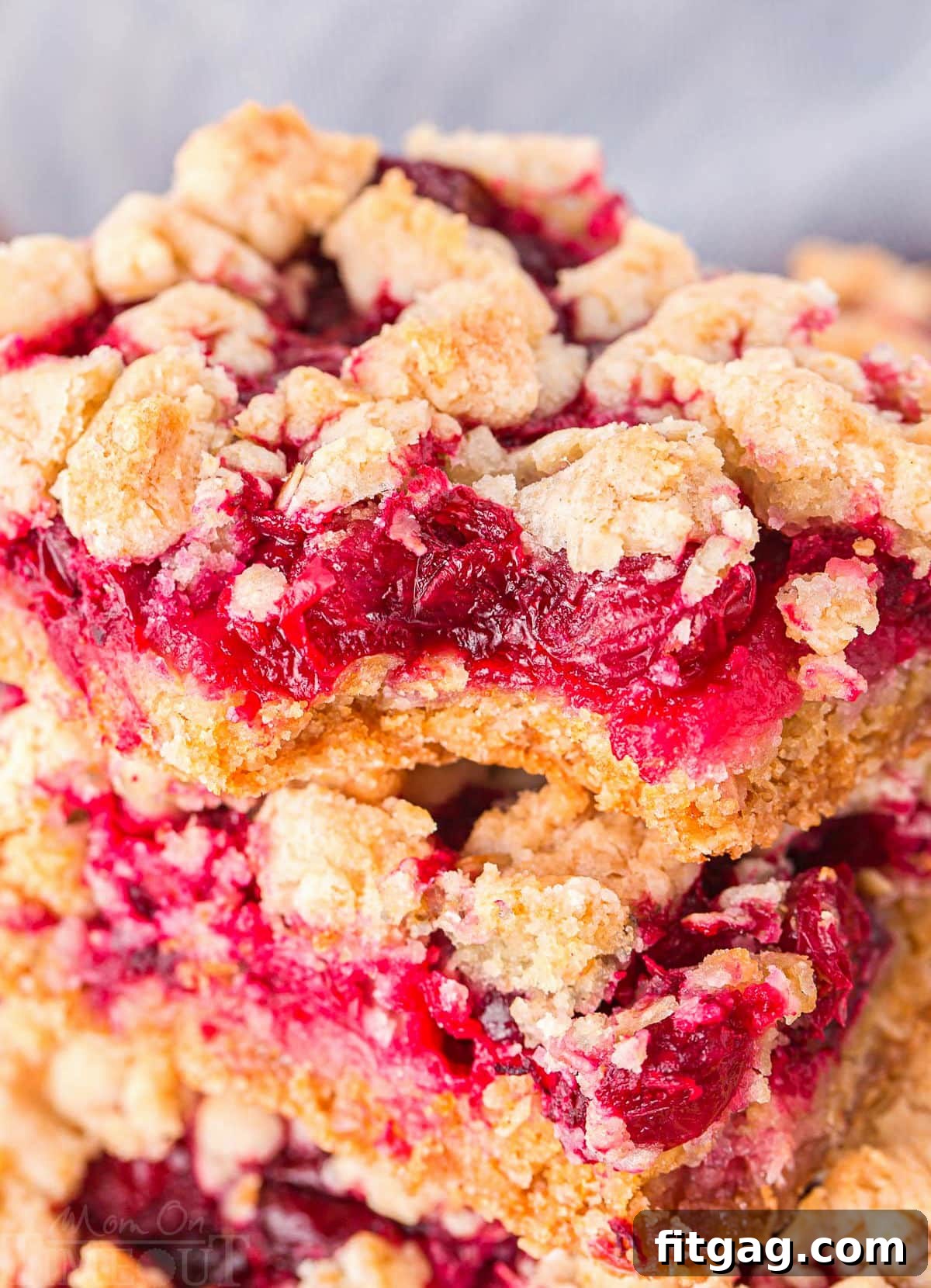 A close-up look at several cranberry bars stacked on top of each other, showcasing the texture of the crumble and the rich color of the filling.