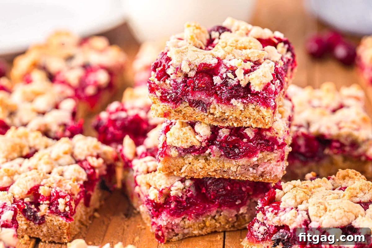 Three cranberry crumb bars stacked on each other on a dark wood board with a glass of milk in the background, inviting and delicious.