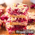 Three cranberry crumb bars stacked on each other on a dark wood board with a glass of milk in the background, a perfect visual for the recipe card.