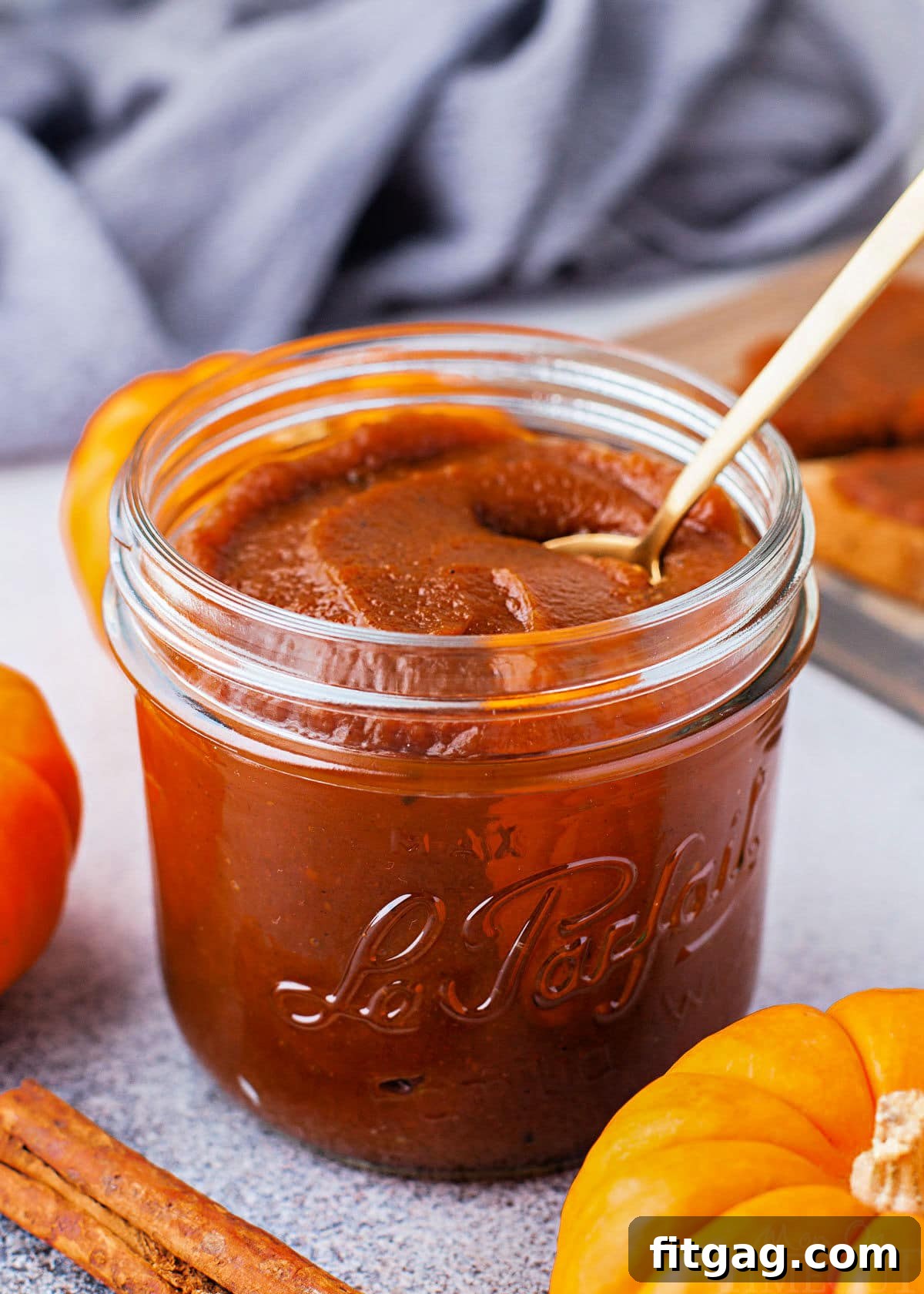 jar of pumpkin butter with small gold spoon sitting in front of a blue napkin. small pumpkin and cinnamon stick are near the jar.