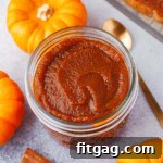 top down look at glass jar filled with pumpkin butter. gold spoon in the pumpkin butter and three small pumpkins surround the jar.