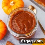 top down look at glass jar filled with pumpkin butter. gold spoon in the pumpkin butter and three small pumpkins surround the jar.