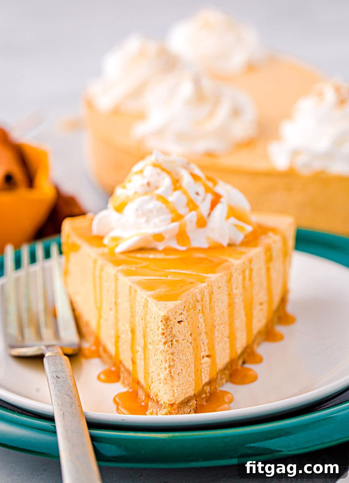 A perfectly sliced piece of no-bake pumpkin cheesecake, elegantly topped with fluffy whipped cream and a luscious caramel drizzle, presented on contrasting white and green plates.