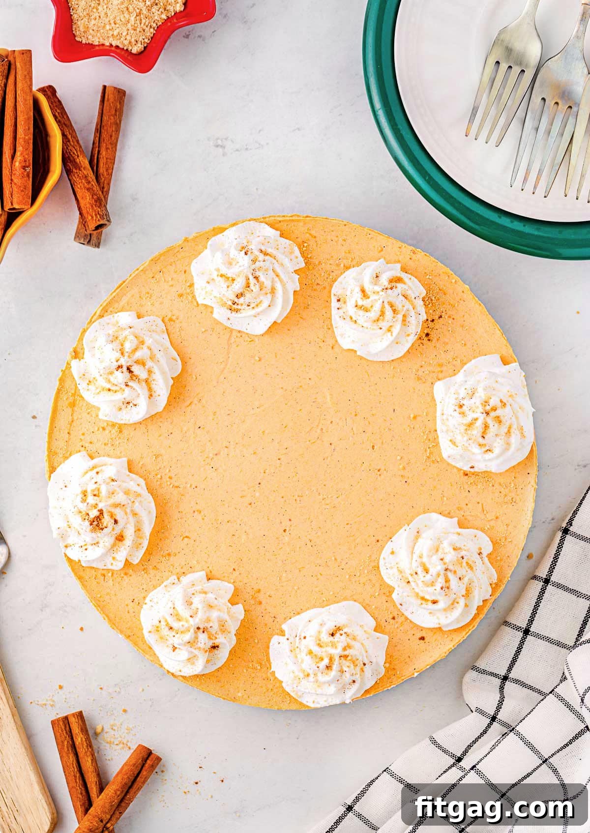 An inviting top-down view of a whole no-bake pumpkin cheesecake, beautifully adorned with evenly spaced dollops of whipped cream, poised for serving.