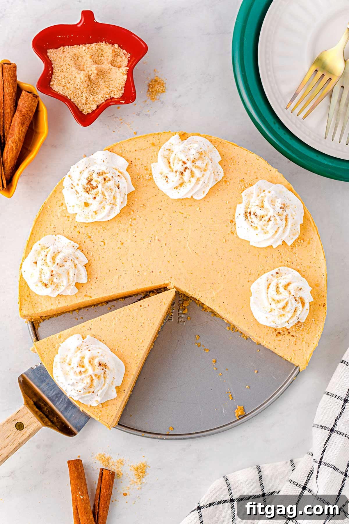 A top-down shot of a no-bake pumpkin cheesecake with decorative whipped cream dollops. One slice has been removed, and another is pre-cut, ready for serving.