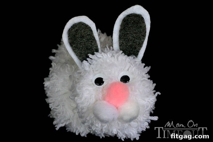 Fluffy Easter Bunny Craft 6 Close-up step-by-step image of gluing eyes, nose, cheeks, and ears onto a pom pom bunny head.