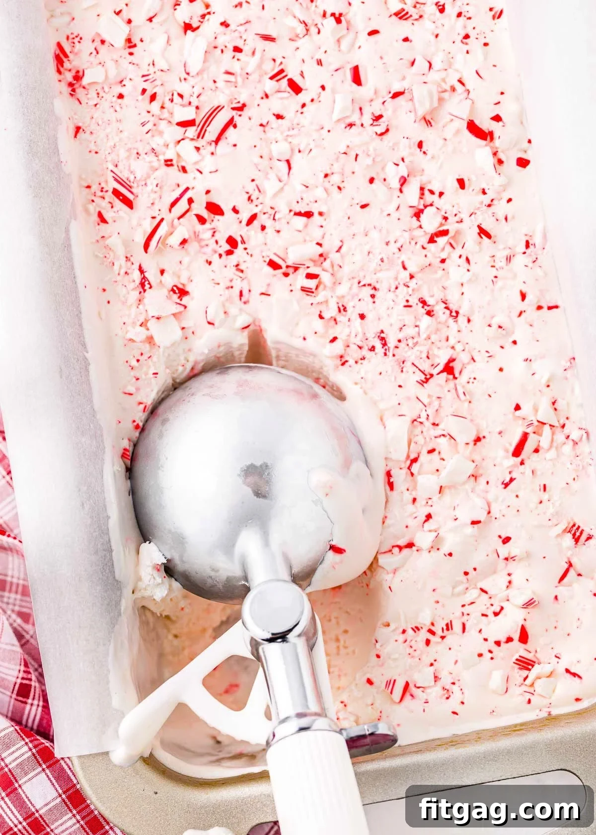 A scoop of rich, creamy peppermint ice cream being lifted from a loaf pan, revealing its beautiful texture and festive color.