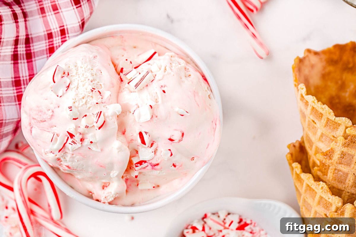 A top-down view of a white bowl overflowing with creamy peppermint ice cream, nestled beside a charming red-and-white checked Christmas linen and two crisp waffle cones.