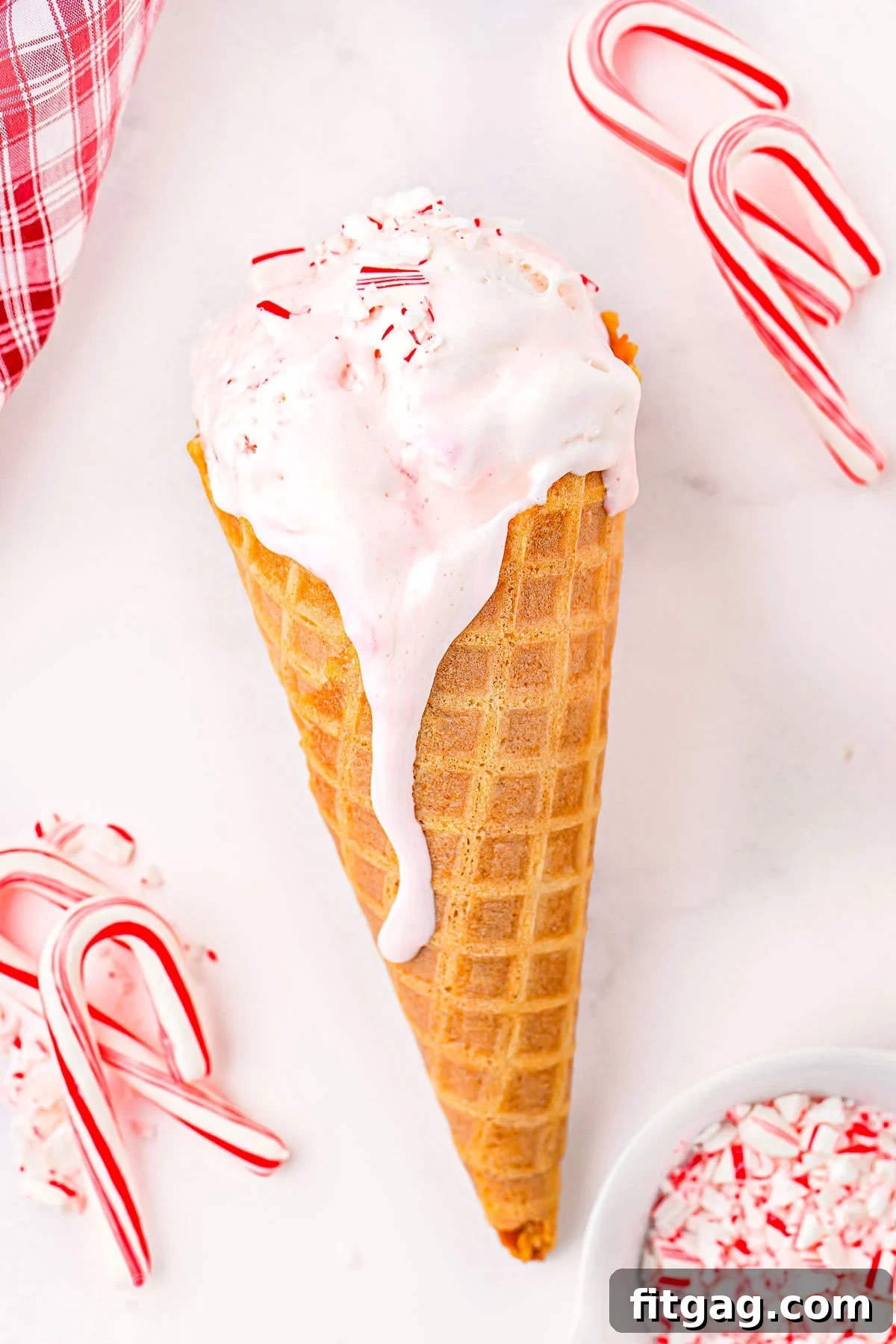 A vibrant scoop of peppermint ice cream nestled in a crispy waffle cone, surrounded by an artful scatter of mini candy canes, creating a delightful and festive visual.