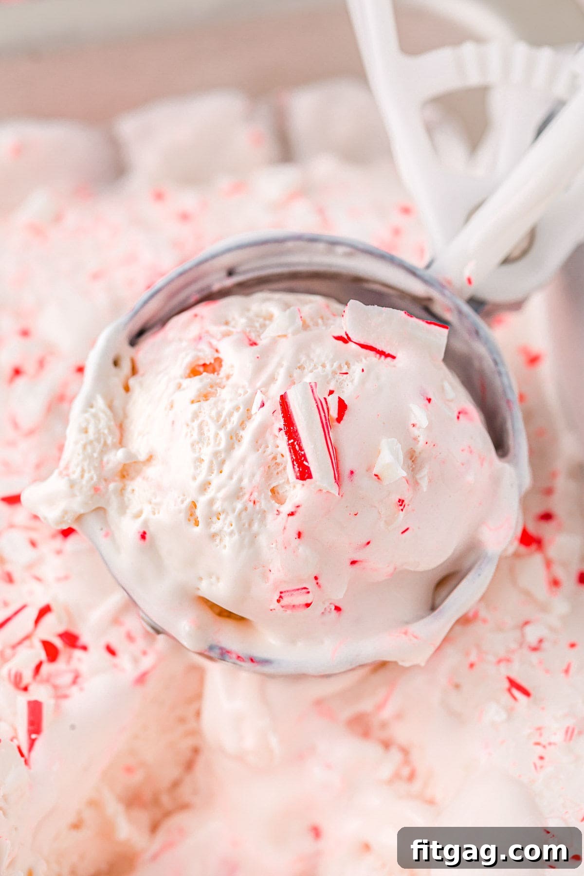 An ice cream scoop generously filled with a perfect scoop of peppermint ice cream, held tantalizingly above the ice cream container, ready to be served.